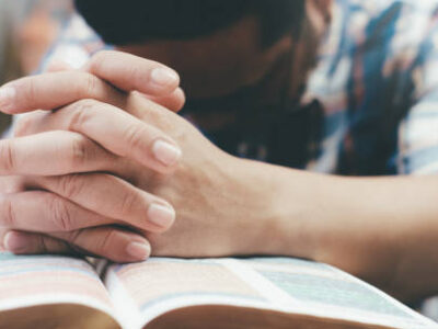 Religion, Christianity, Praying.  Man praying, hands clasped together on her Bible.